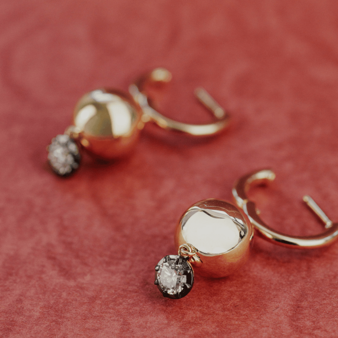 14k gold round cut, lab grown diamond dangle/hoop earrings with Black Rhodium featured on a textured red surface.  