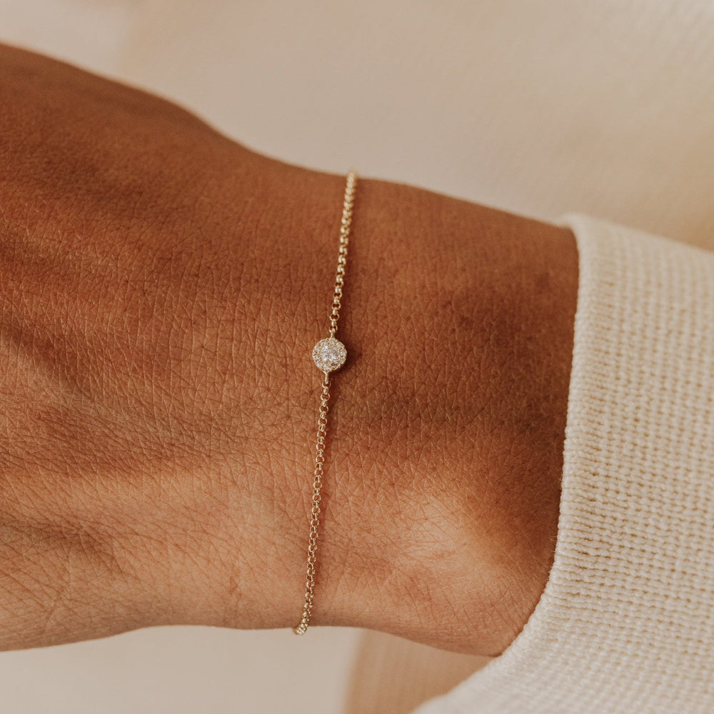 Gold bracelet with a diamond on a wrist against a neutral background.