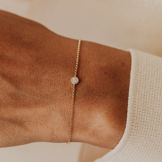 Gold bracelet with a diamond on a wrist against a neutral background.