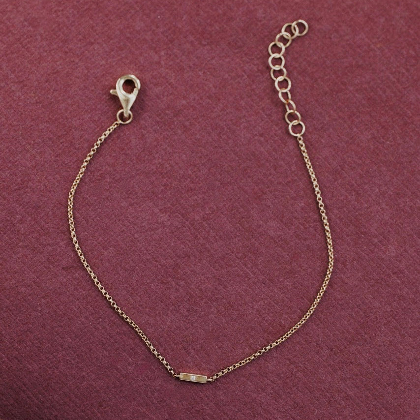 A delicate gold chain bracelet with a lobster clasp and an adjustable extension chain, displayed on a textured dark pink fabric background.