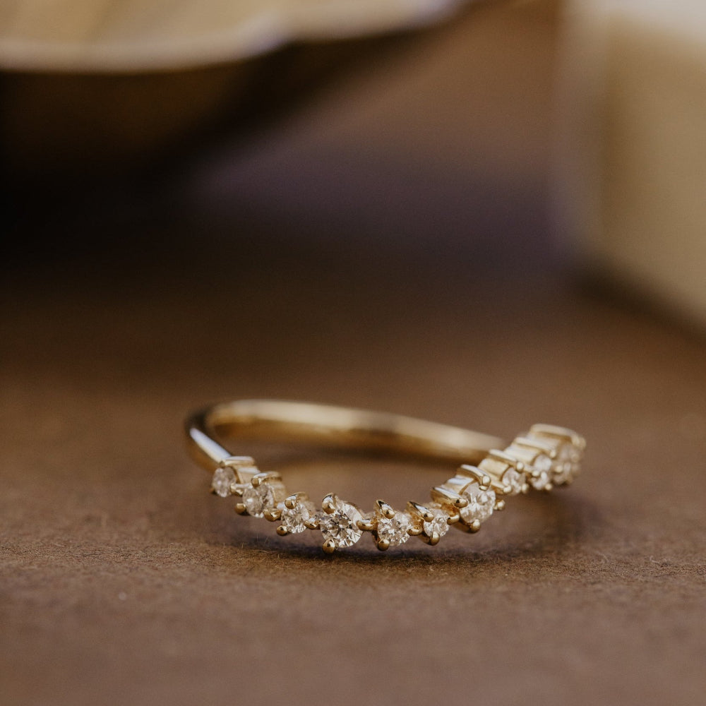 Gold wave-shaped wedding band with diamond accents on a brown surface.