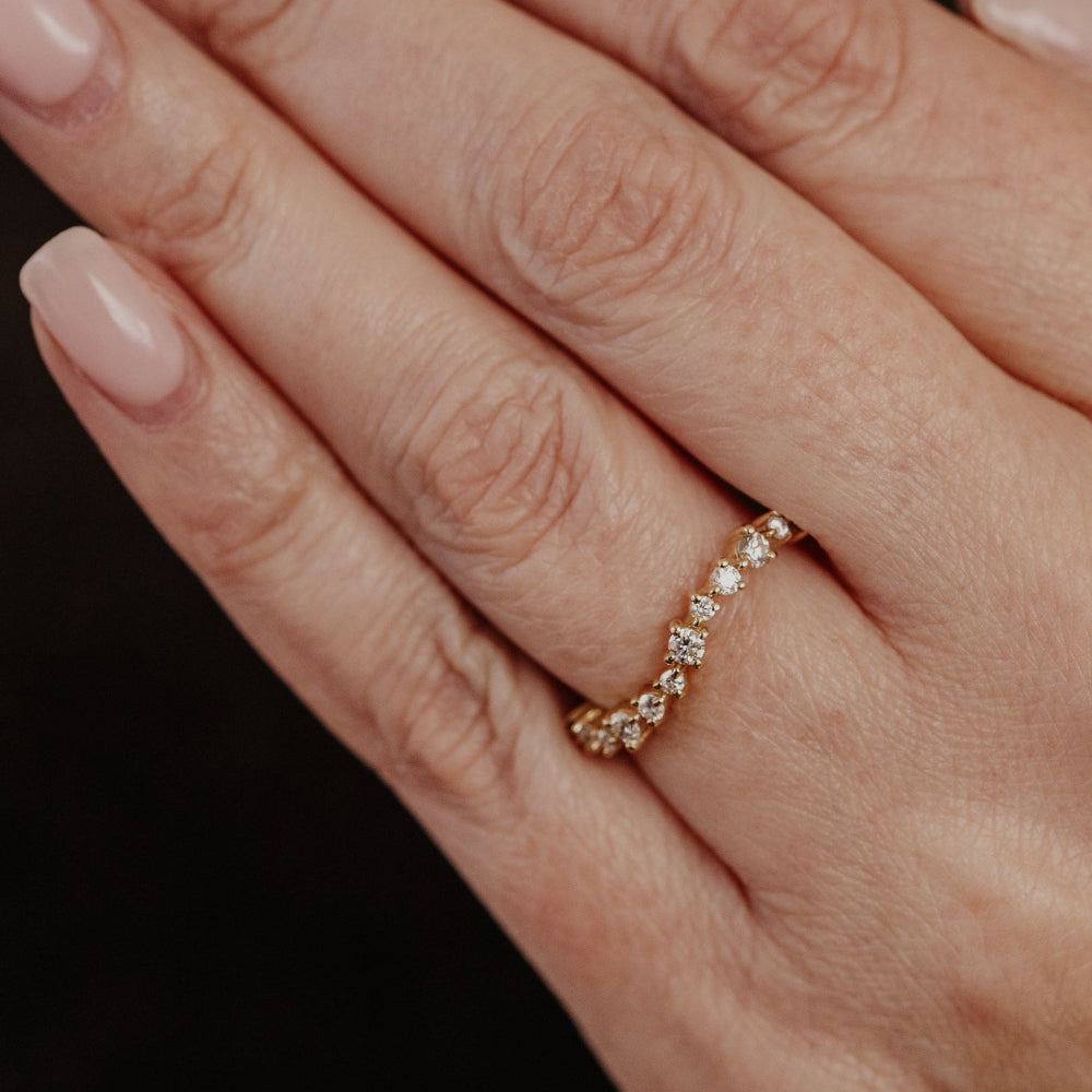 Yellow gold wedding band with diamonds on a hand against a dark background.