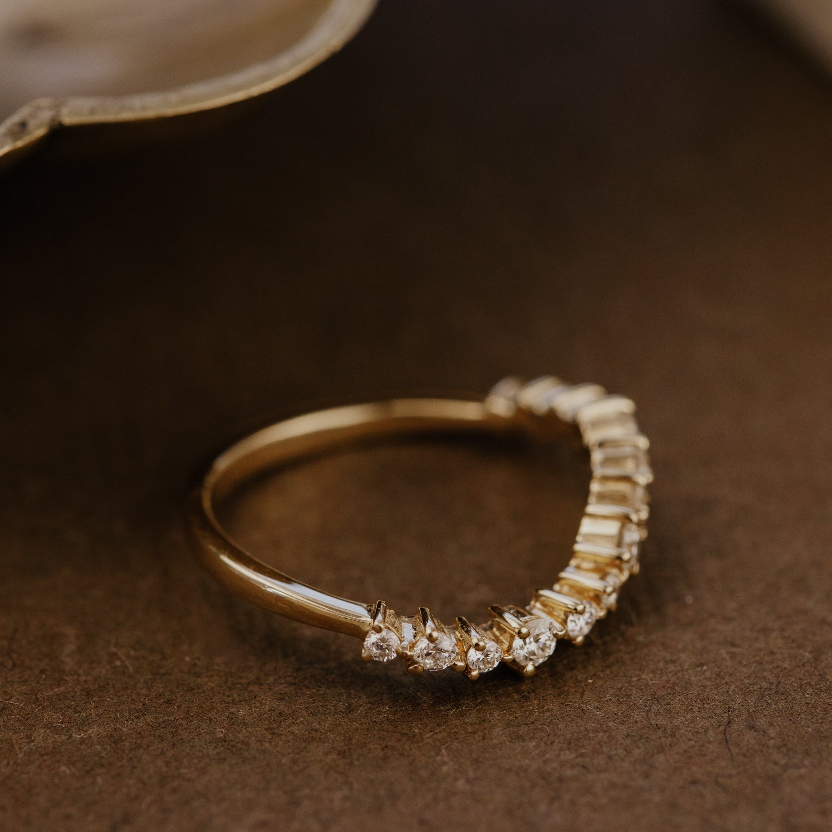Gold wedding band with small diamonds on a brown surface.