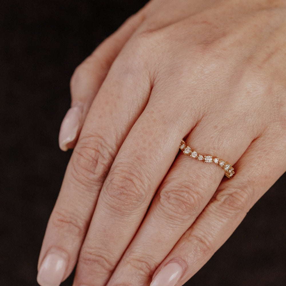 Close-up of a hand wearing a yellow gold wedding band with round diamonds on a dark background.