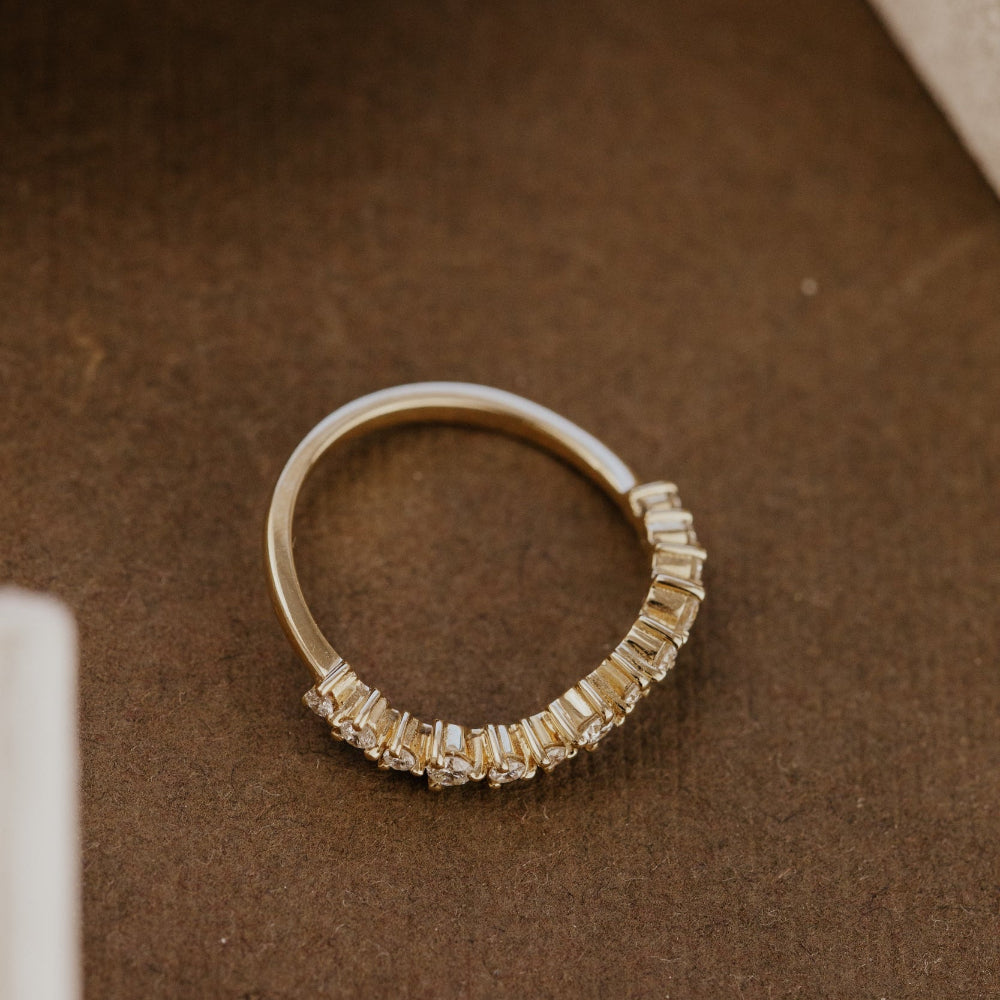 Gold wedding band with diamond accents on a brown surface.