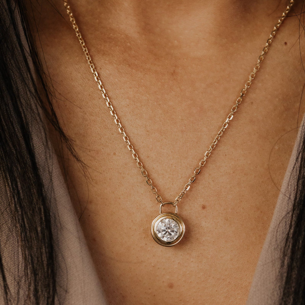 Gold necklace with a round land grown diamond pendant on a person's neck.