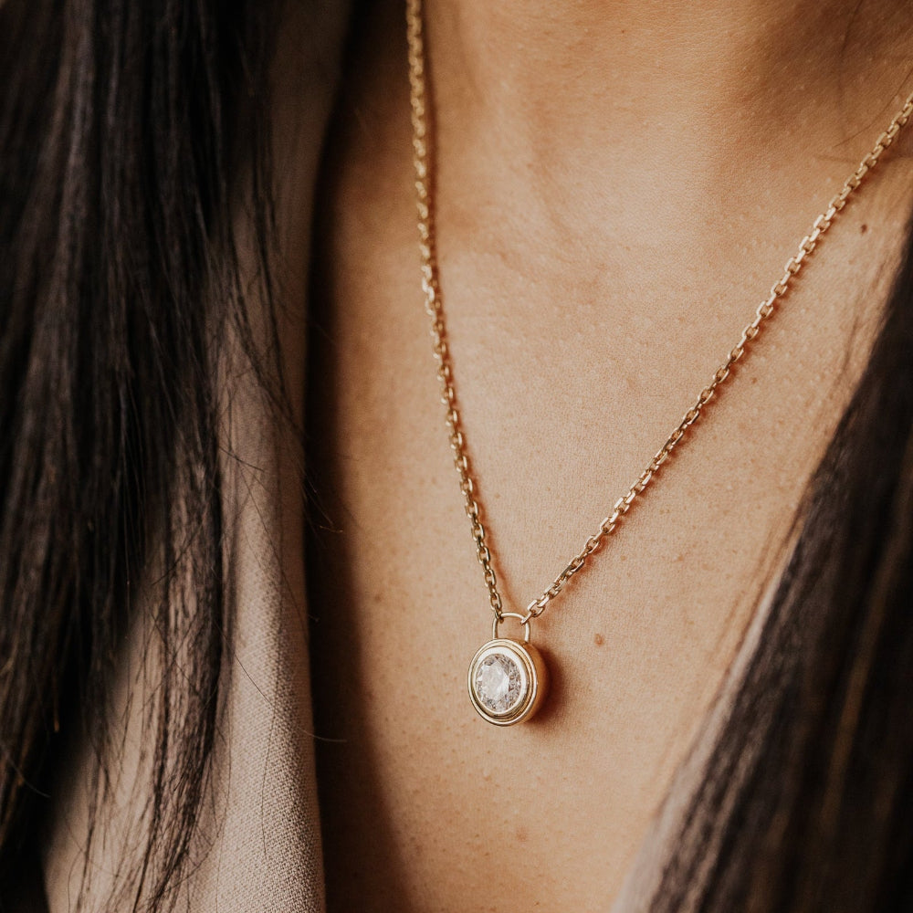 Gold necklace with a round lab grown diamond pendant on a person's neck.