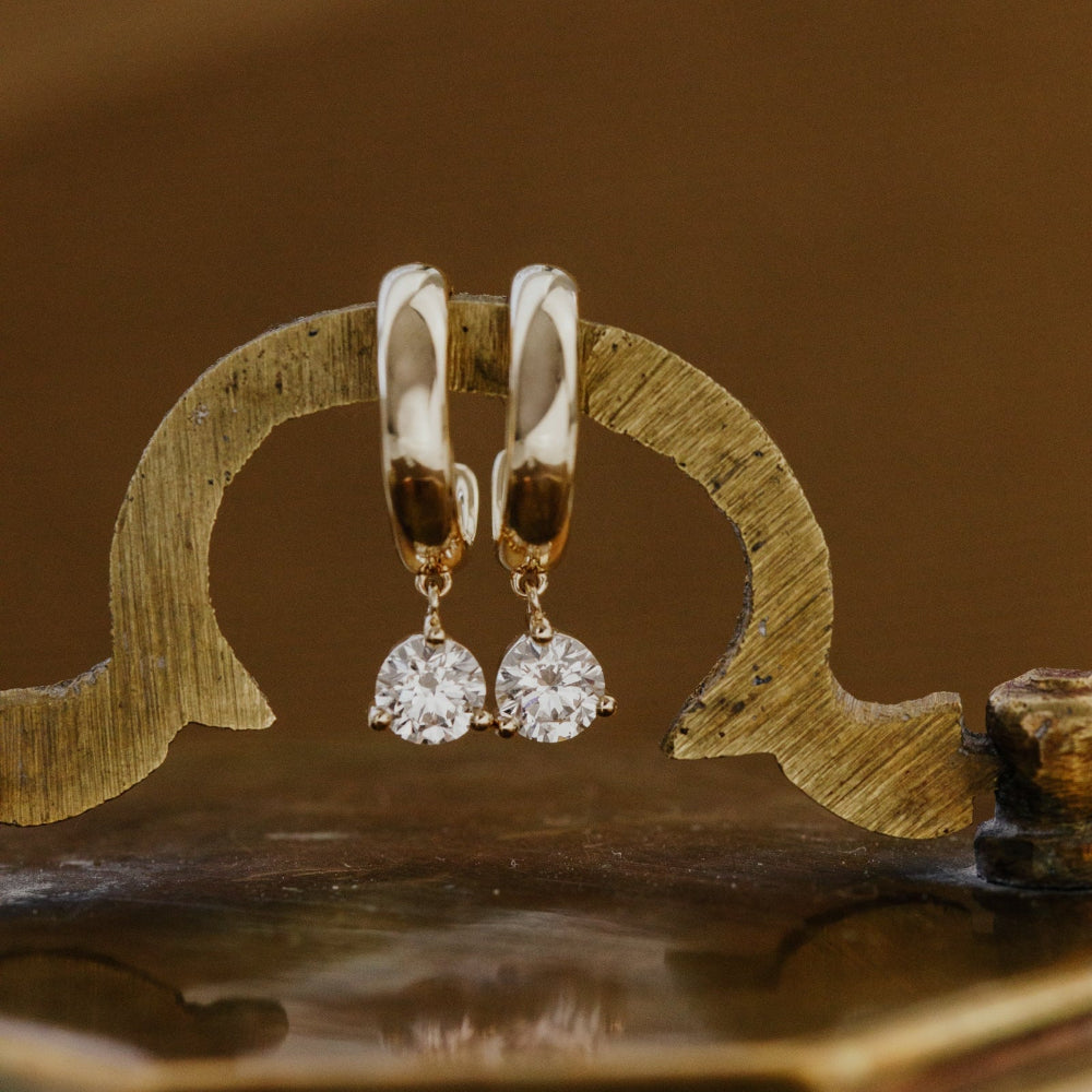 Gold hoop earrings with round lab grown diamond dangles on a decorative wooden stand.