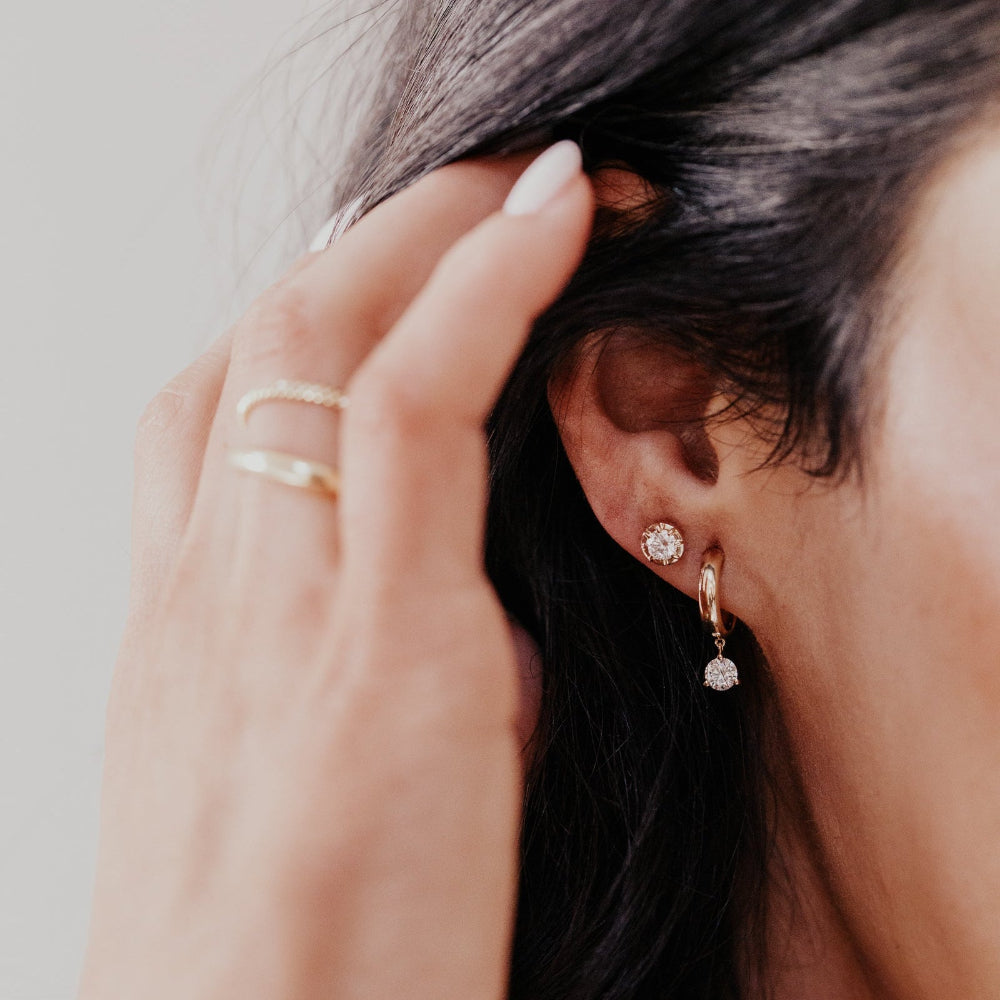 Close-up of a person wearing gold hoop earrings with round lab grown diamond dangles a neutral background.