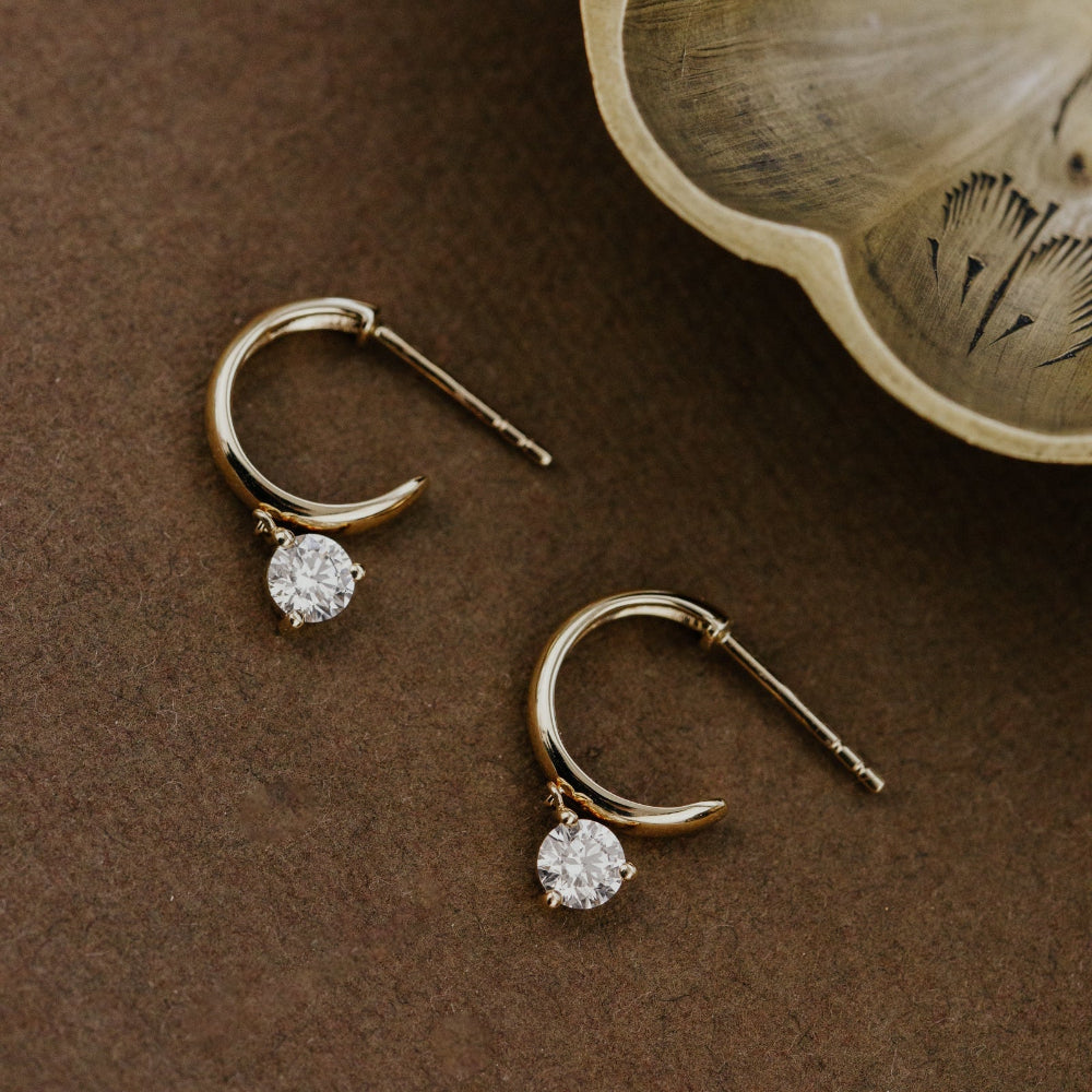 Gold hoop earrings with small round lab grown diamonds on a brown surface with a wooden bowl.