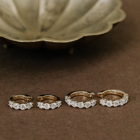 Set of gold hoop earrings with lab grown diamond accents on a brown surface.
