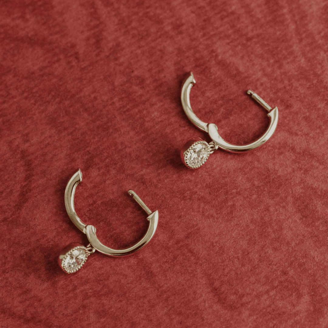 14k gold diamond earrings with a bezel design with huggie and dangle designs showcased on a textured red surface. 