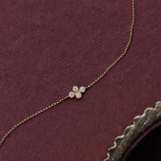 A delicate gold chain necklace featuring a diamond cluseter, displayed on a textured dark burgundy fabric background.