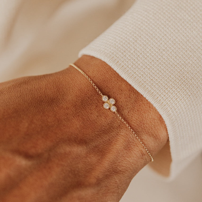 A delicate gold chain bracelet with a round diamond cluster shown worn on a person's wrist against a soft cream-colored knit sleeve.