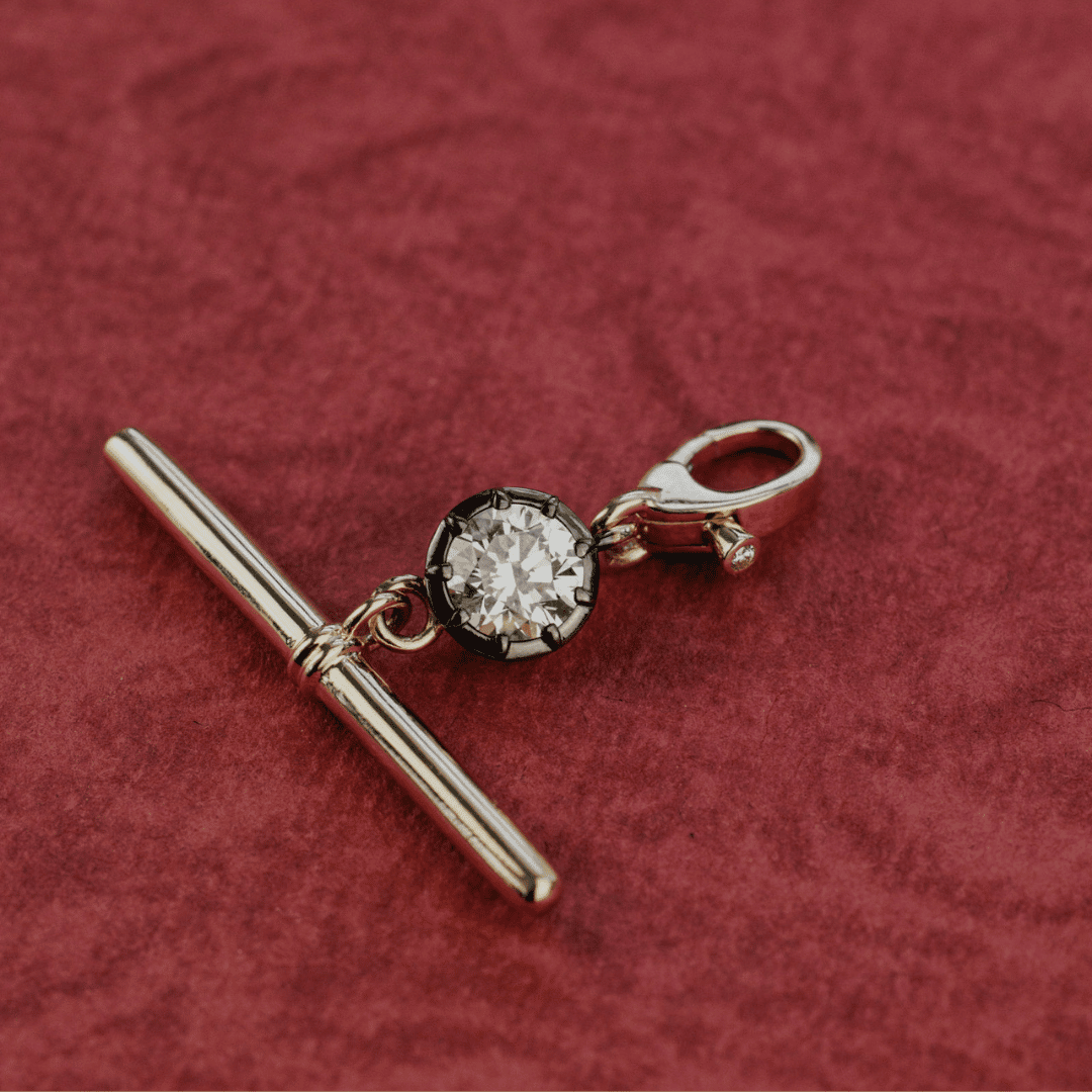A Round cut Lab Grown Diamond with a Black Rhodium Round Ball Dog Clip shown on a red textured surface. 