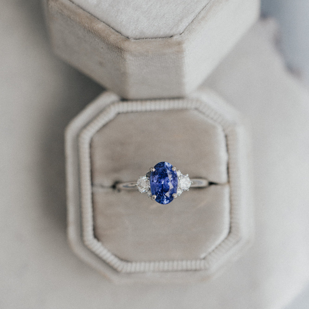 Ring with a blue sapphire in a hexagonal jewelry box on a light gray background
