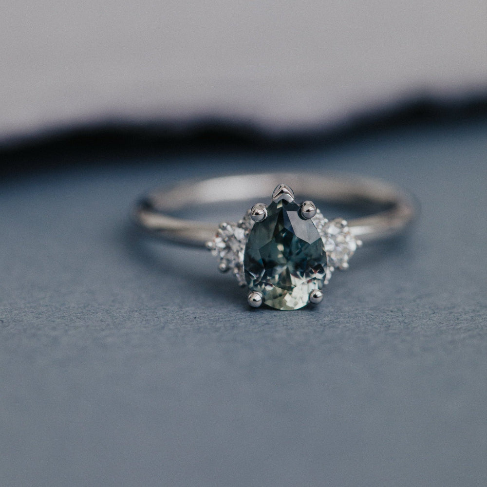 white gold ring with a green gemstone on a gray surface