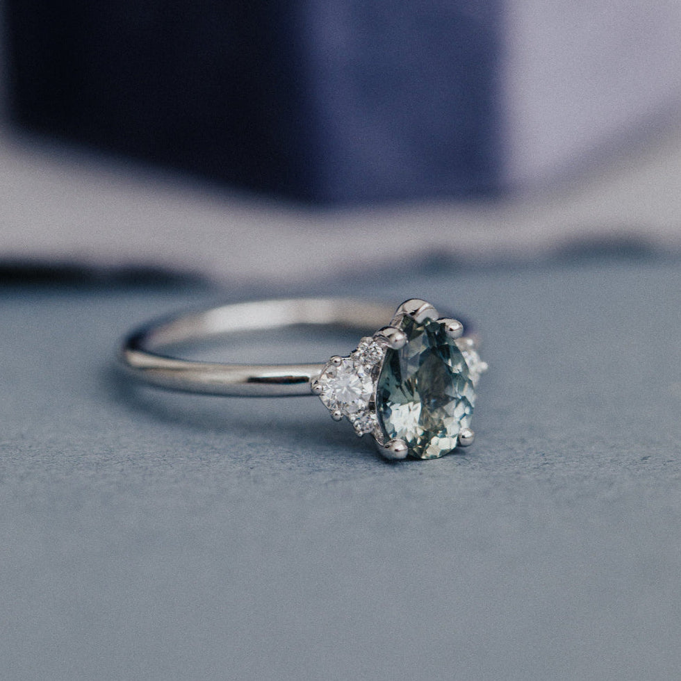 White gold ring with a green sapphire gemstone on a gray surface