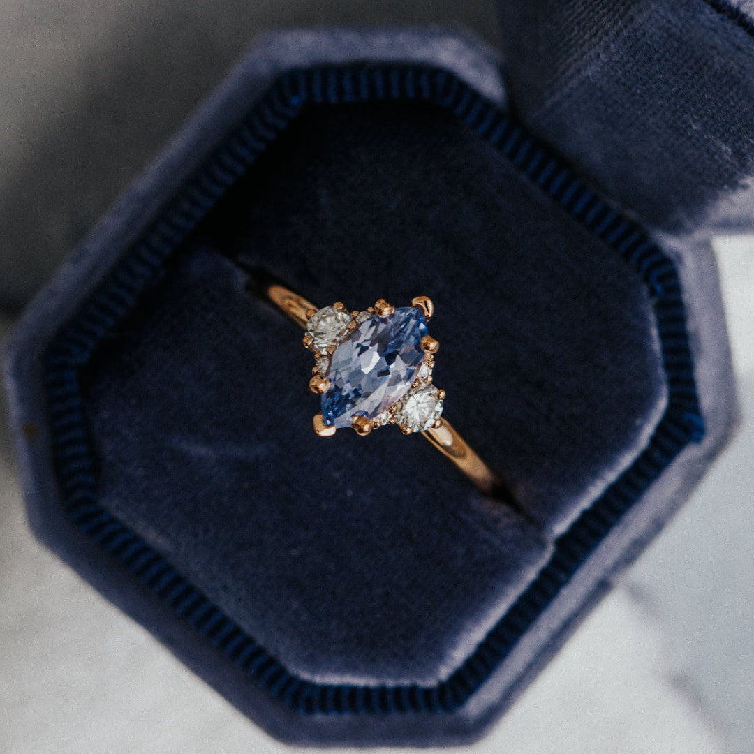 Gold ring with a blue sapphire gemstone in a navy velvet box on a gray background