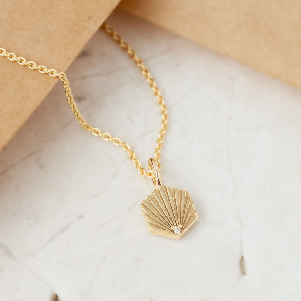 Gold necklace with a shell pendant on a marble surface