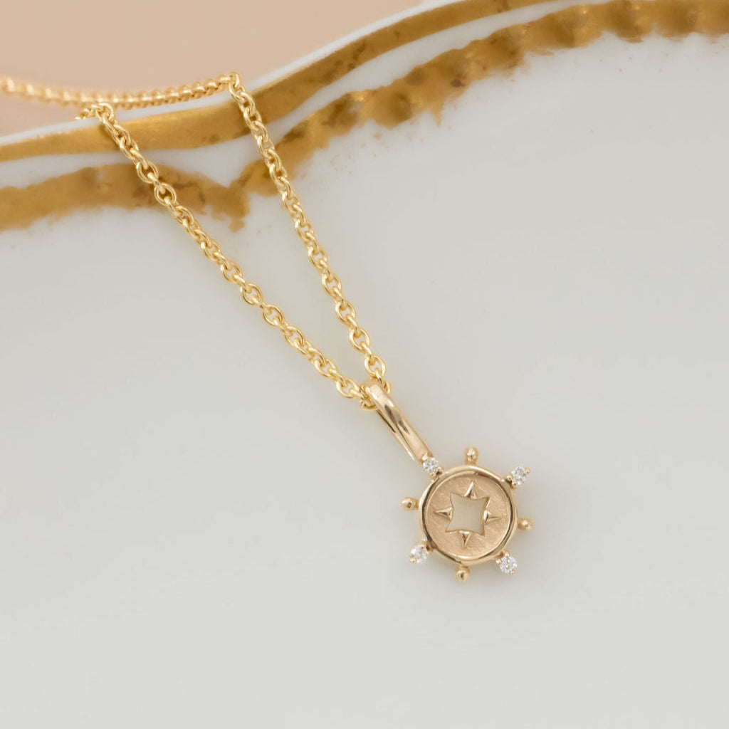 Gold necklace with a small charm with diamond accents on a light background