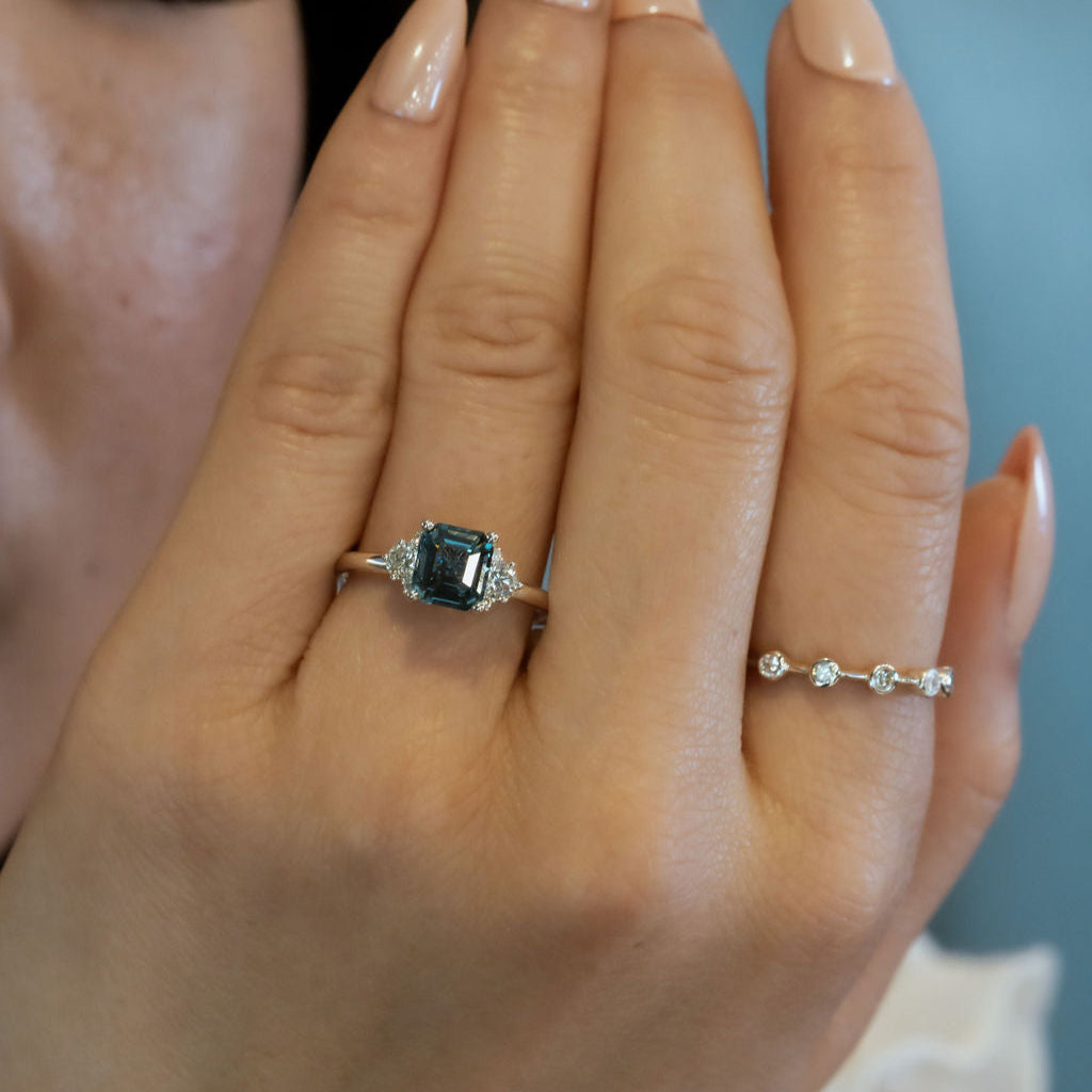 Hand wearing a ring with a blue Montana Sapphire and another ring on a neutral background