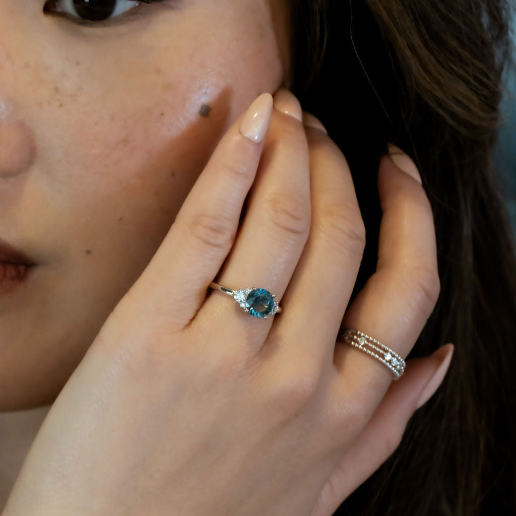 Close-up of a hand with a blue Montana Sapphire ring, touching the face.