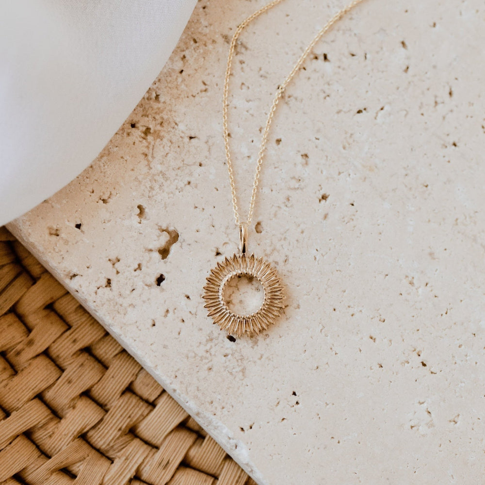 Gold necklace with a circular pendant on a textured surface