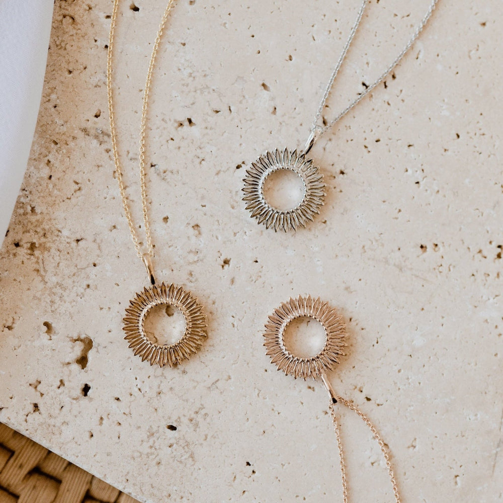 Three gold-colored necklaces with an open circle design and textured petals around the outer edge, displayed on a textured background.