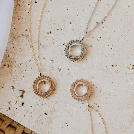 Three gold-colored necklaces with an open circle design and textured petals around the outer edge, displayed on a textured background.