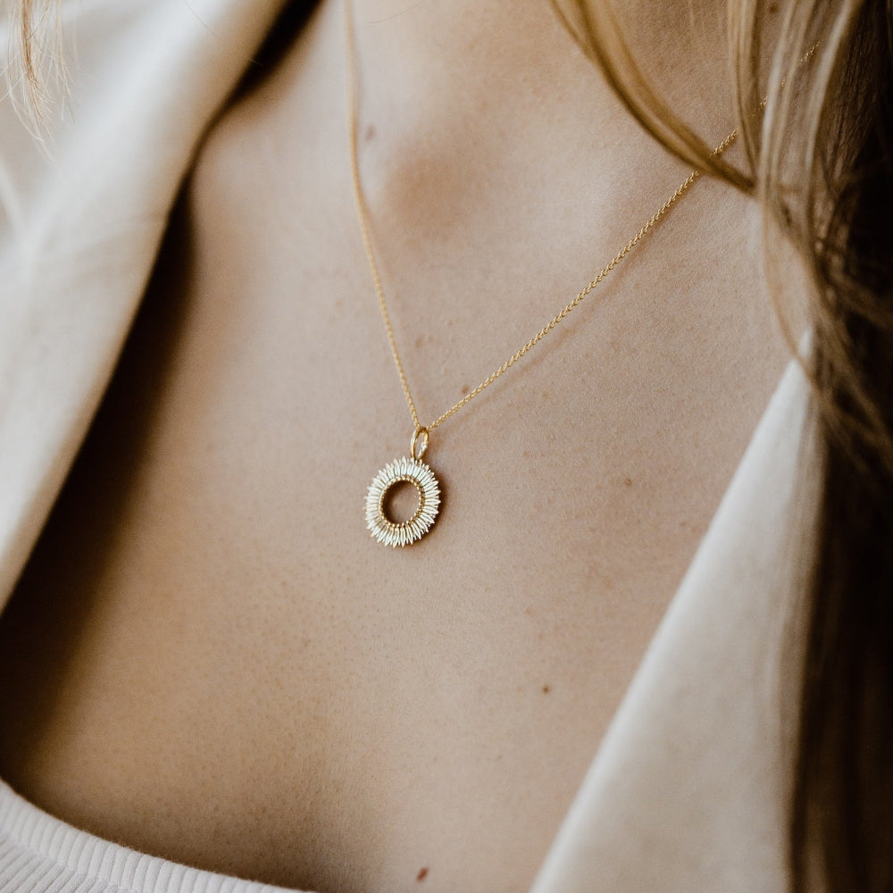 Gold necklace with a circular pendant on a person wearing a white top.