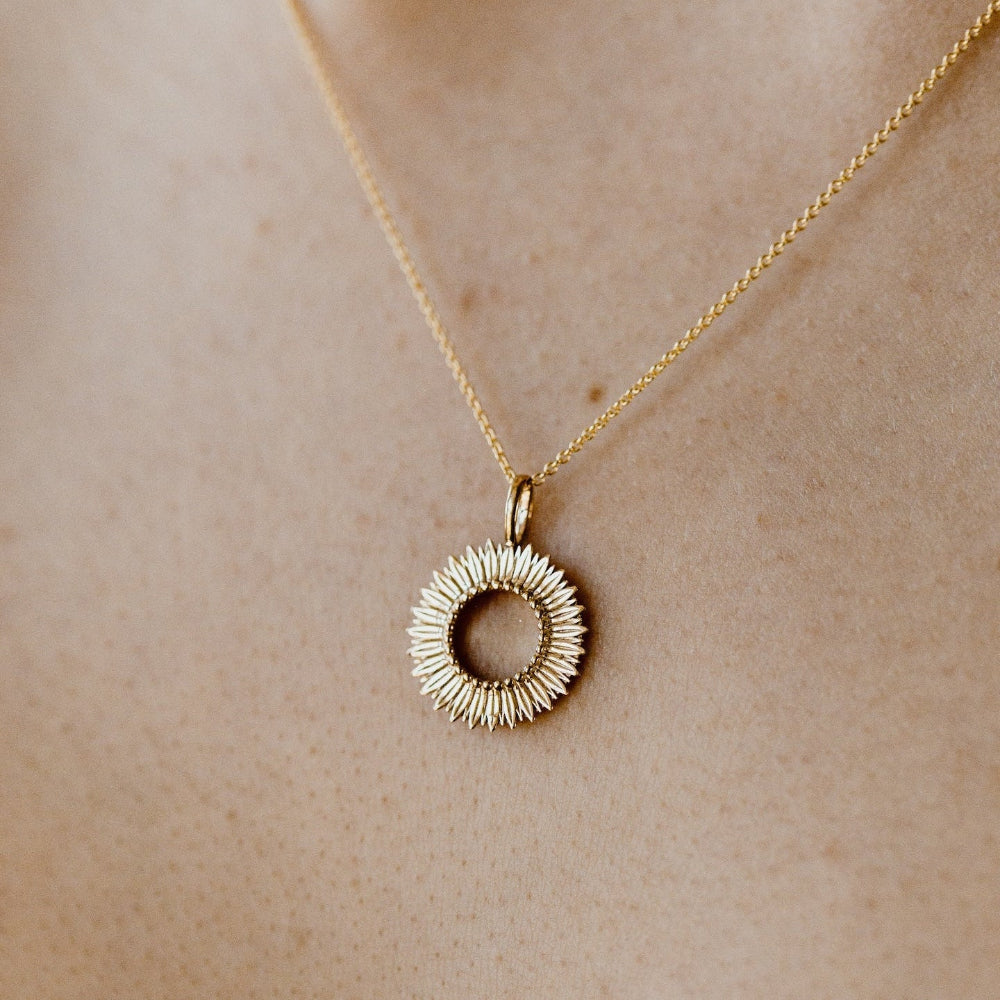 Gold necklace with a circular pendant on a neutral background