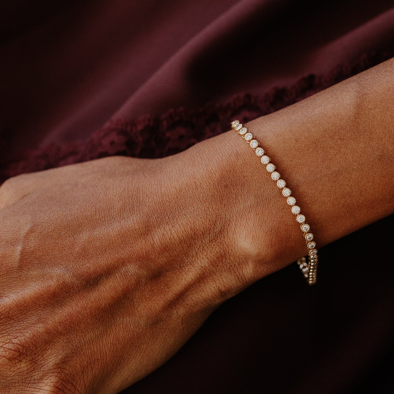 Close-up of a wrist wearing a diamond tennis bracelet against a dark fabric background