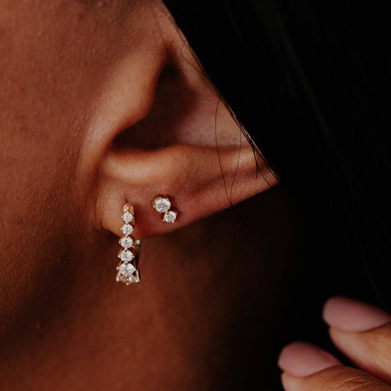 Close-up of an ear wearing diamond earrings with a dark background