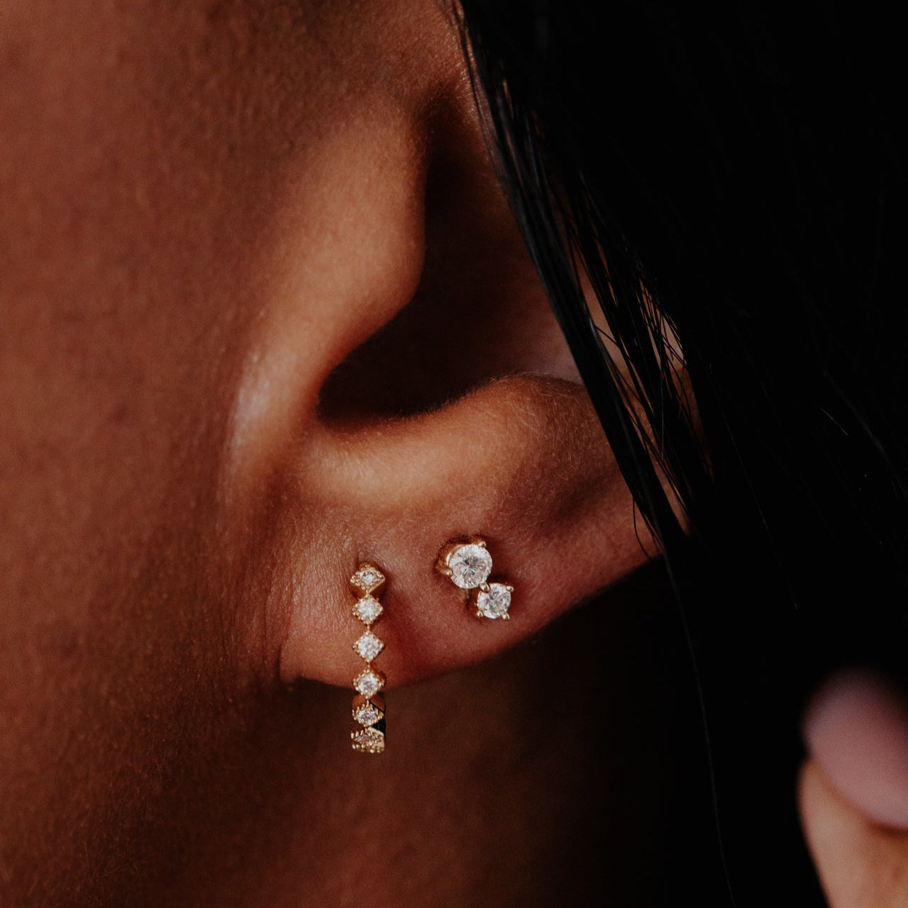 Close-up of an ear wearing diamond earrings with a dark background