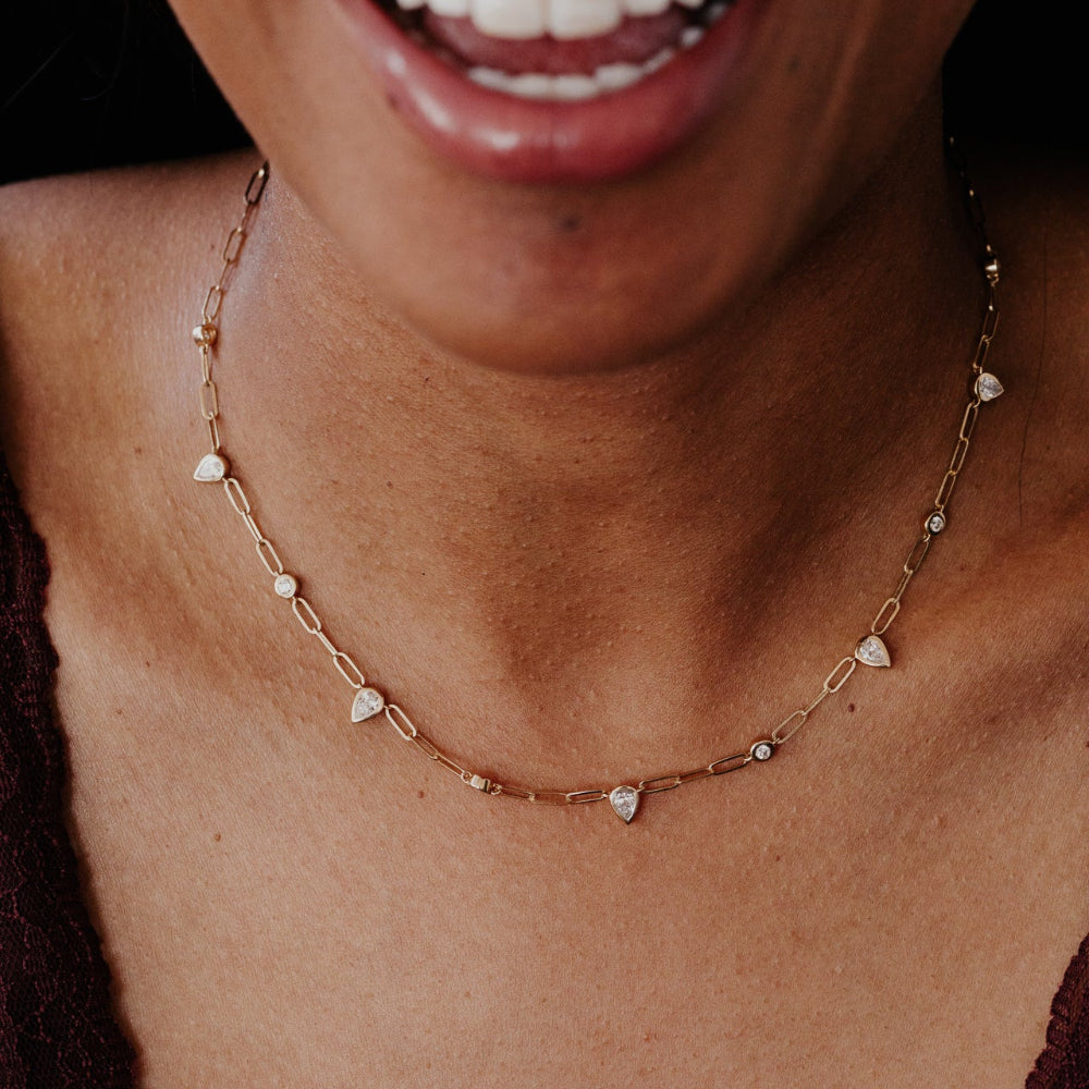 Close-up of a person wearing a delicate gold necklace with pear-shaped diamond pendants.