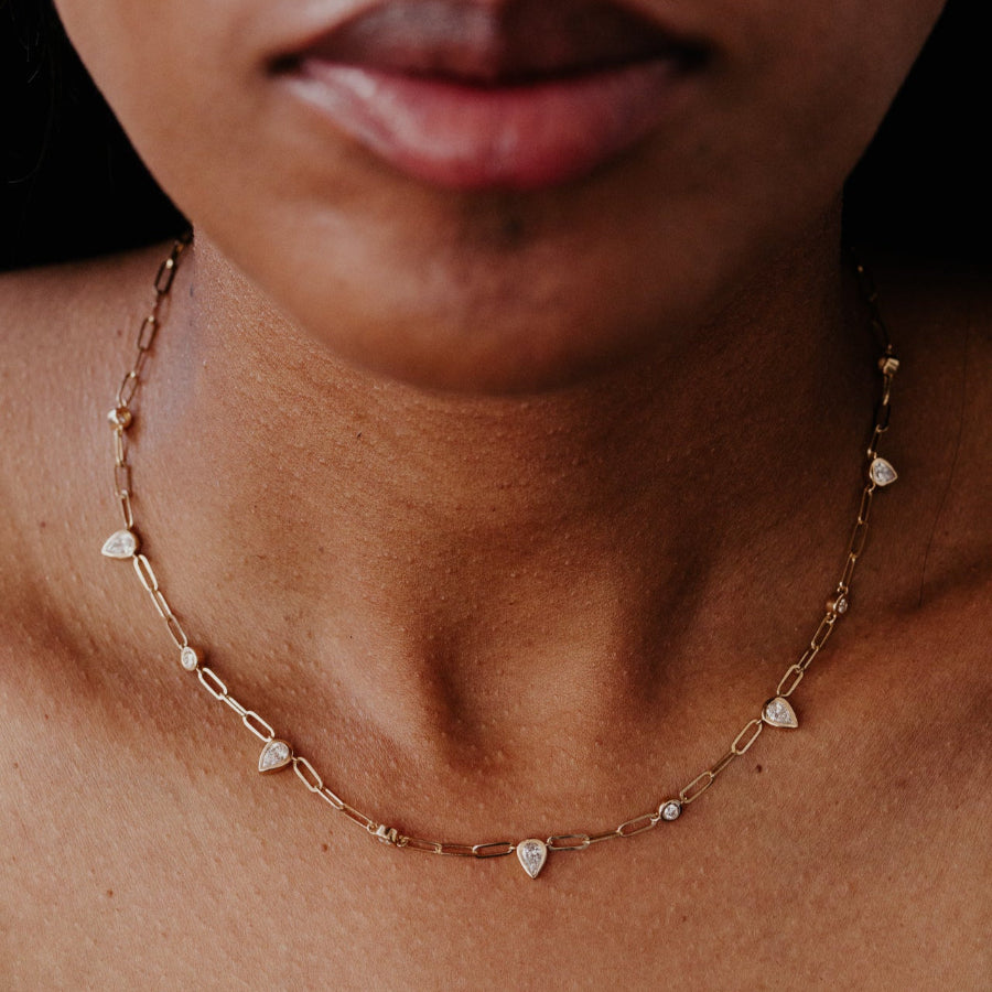 Close-up of a gold necklace with pear-shaped diamond pendants on a person's neck.