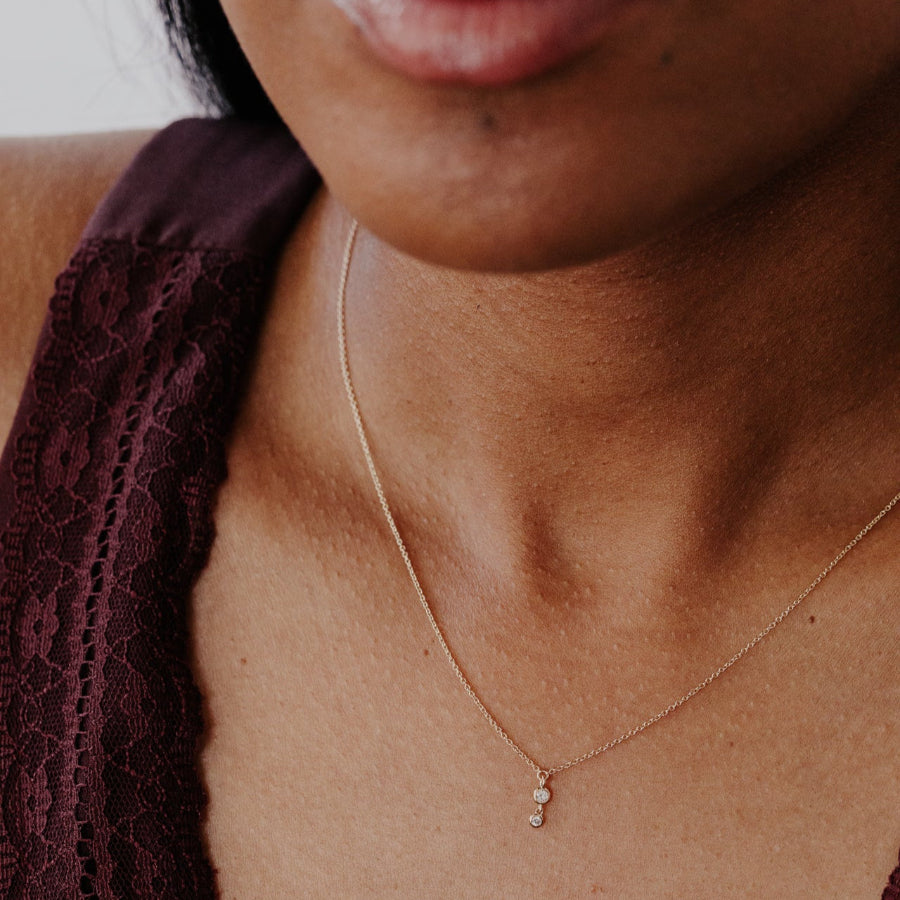 Close-up of a person wearing a gold necklace with a small diamond pendant.