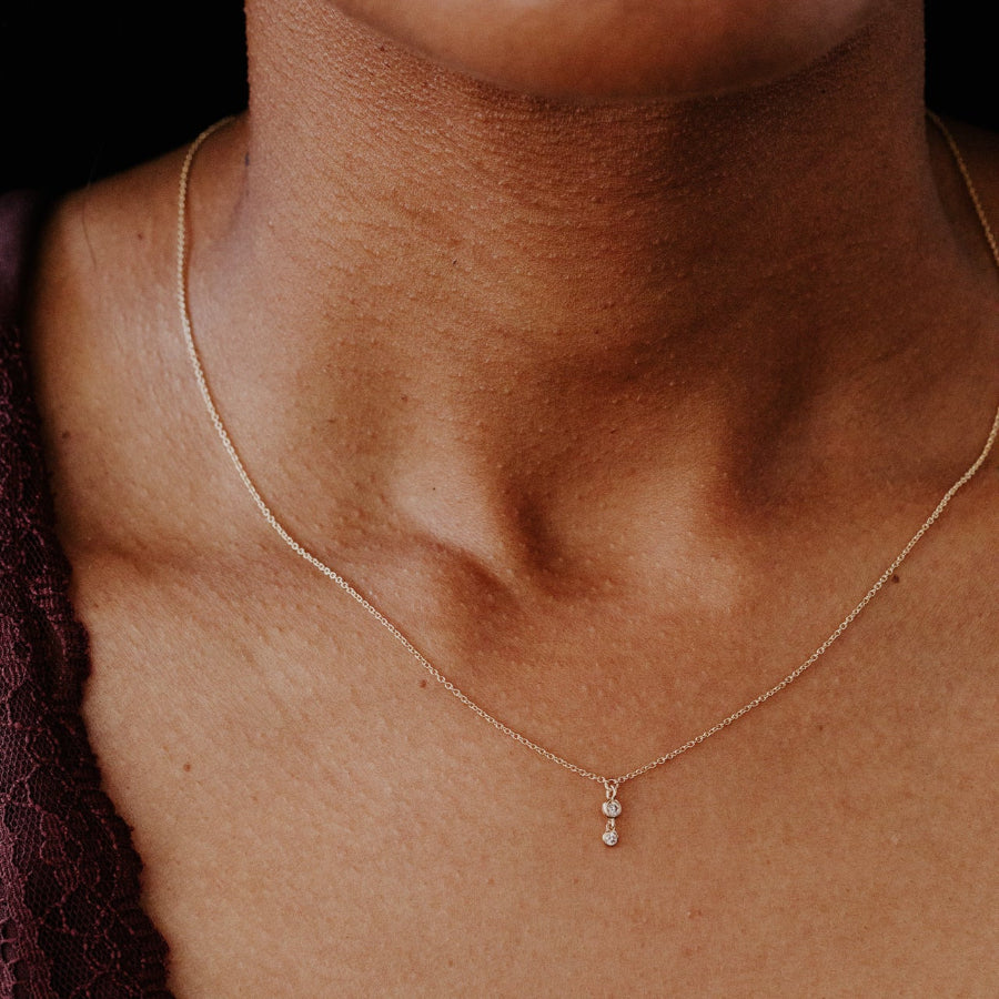 Necklace with a small diamond pendant on a person's neck against a dark background