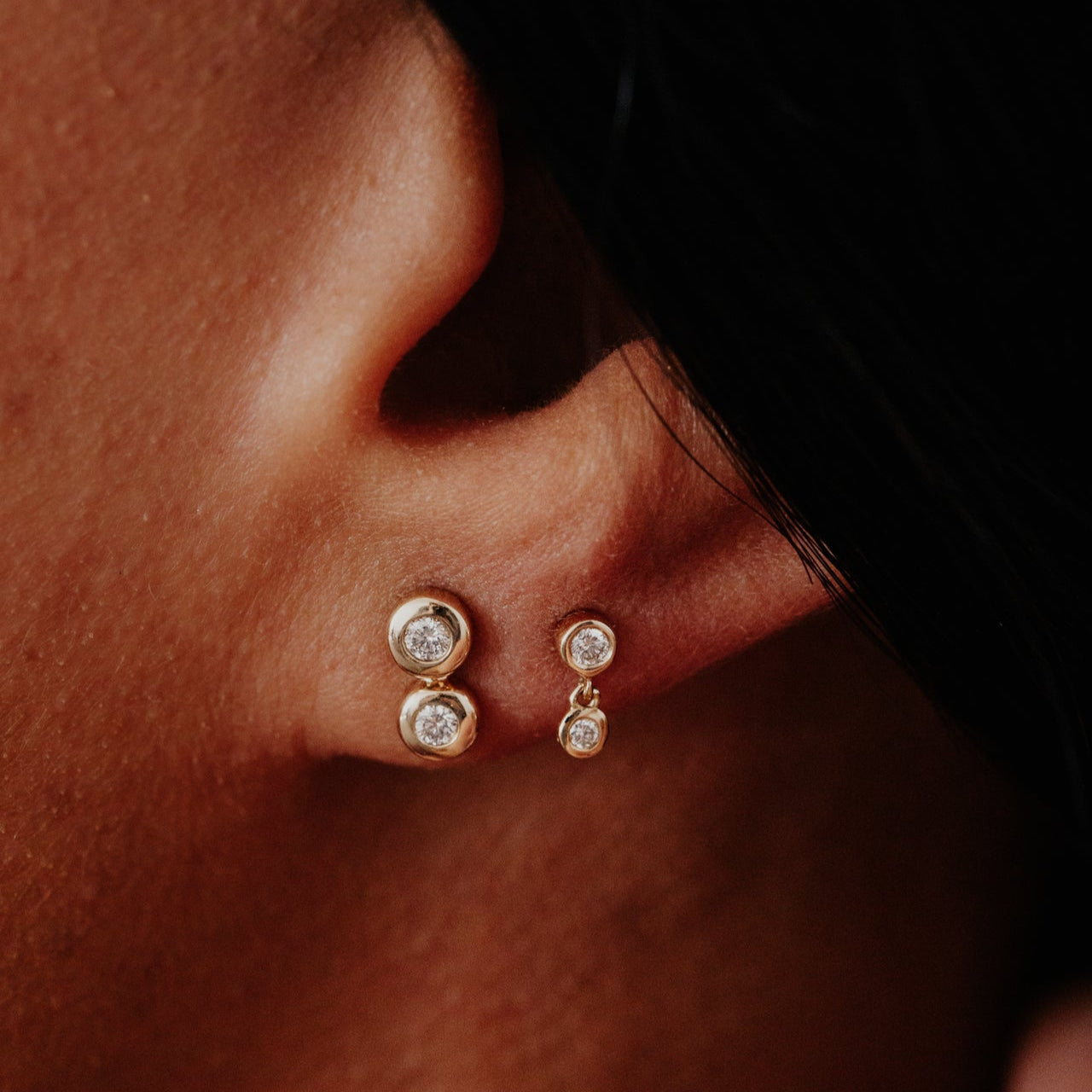 Close-up of gold earrings with diamonds worn on an ear.