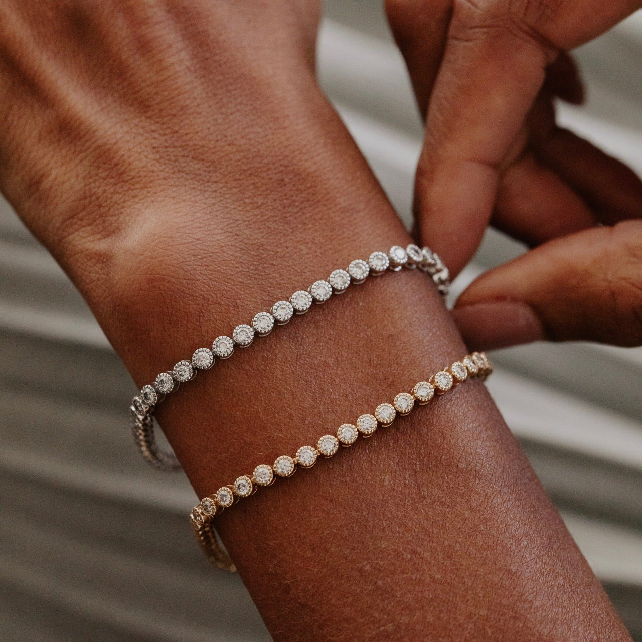 Close-up of a person's wrist wearing two diamond tennis bracelets on a neutral background