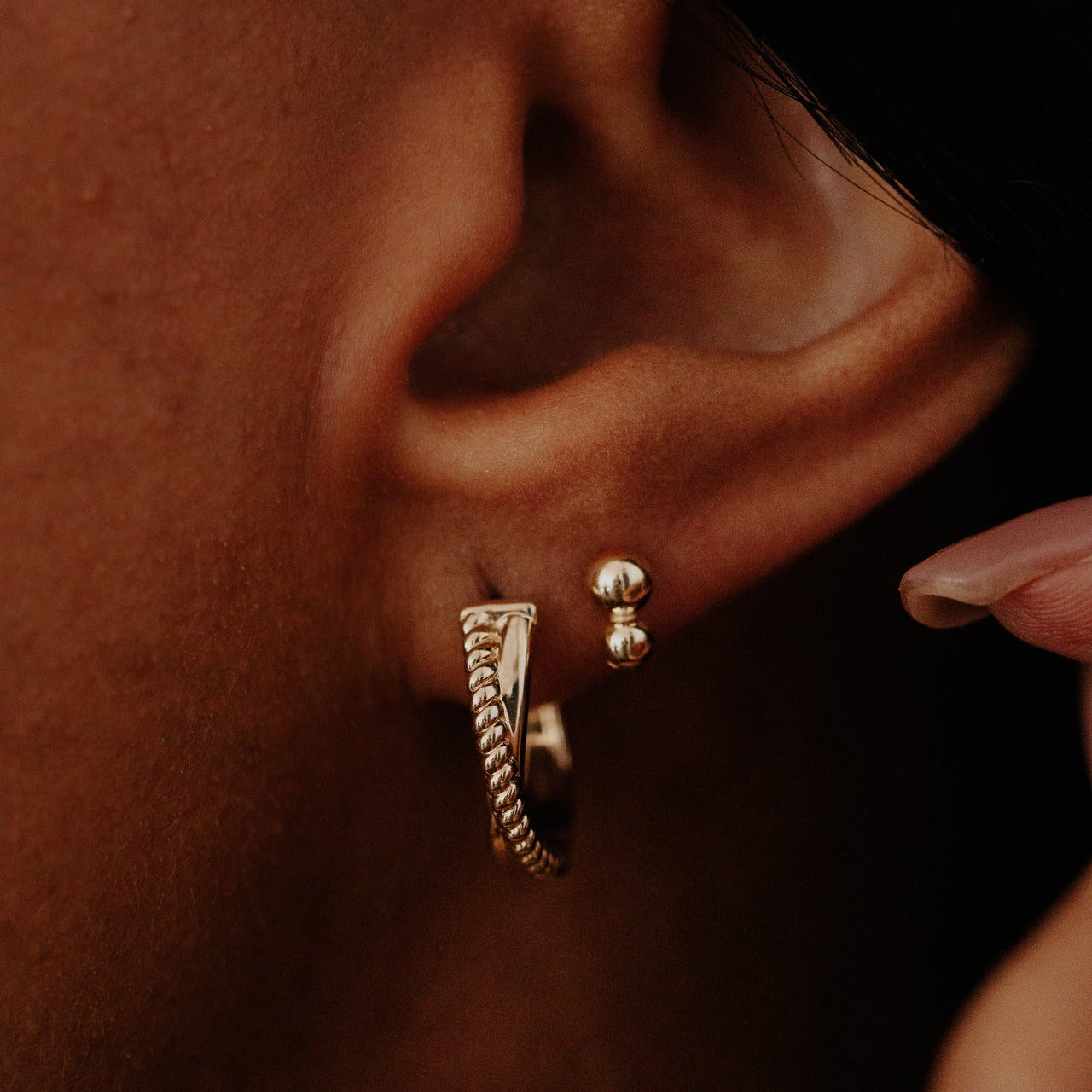Close-up of an ear wearing gold hoop earrings with a dark background