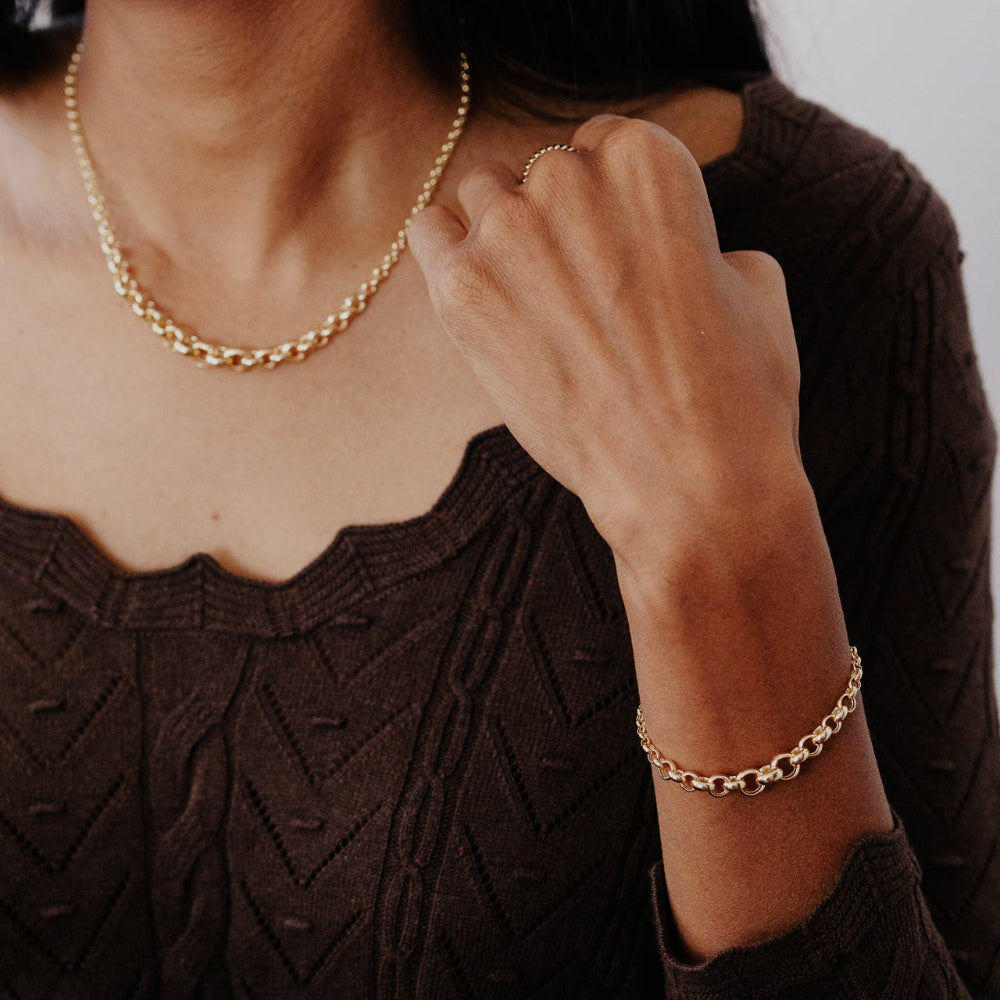 Person wearing a gold necklace and bracelet, with a blurred background