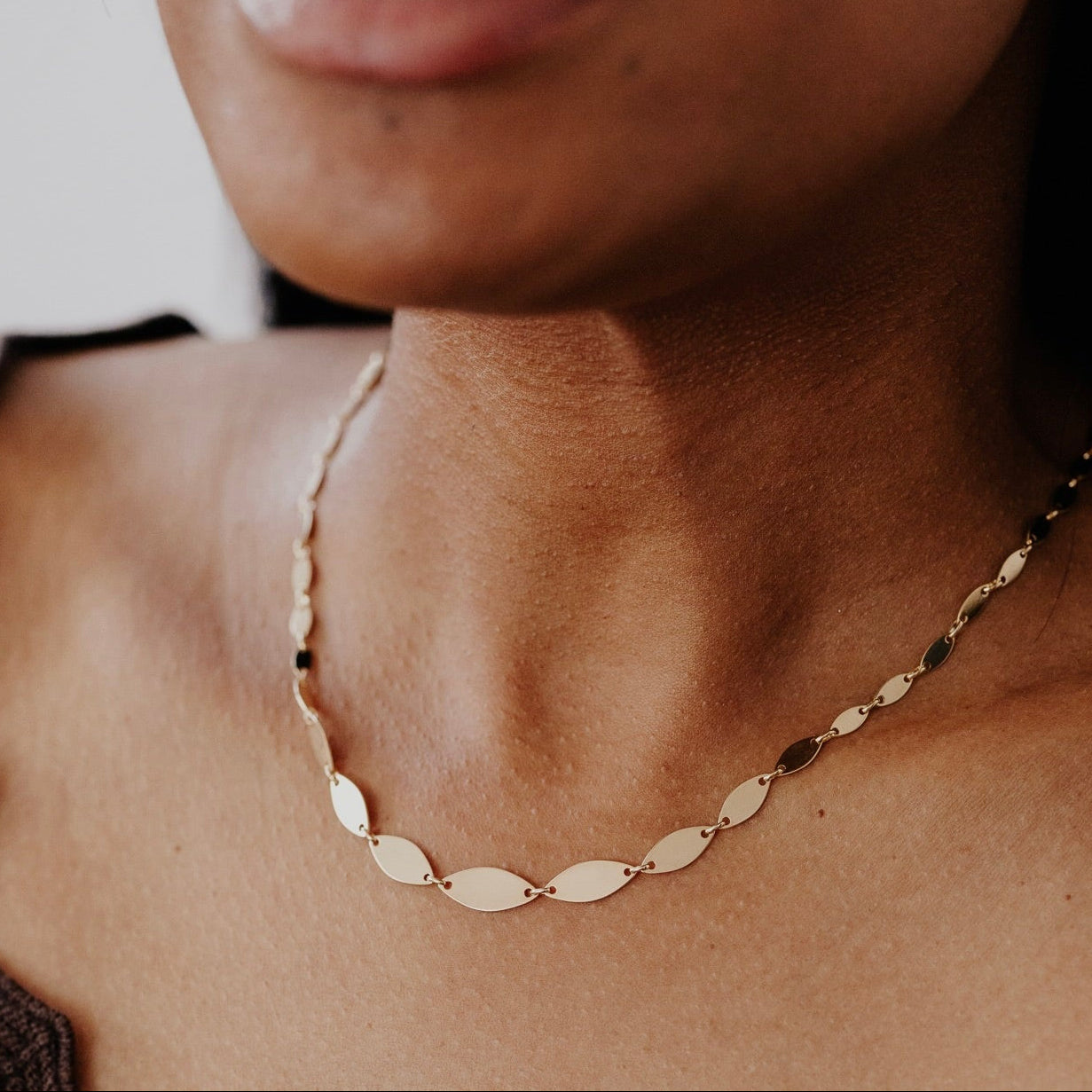 Close-up of a person wearing a gold necklace with a blurred background
