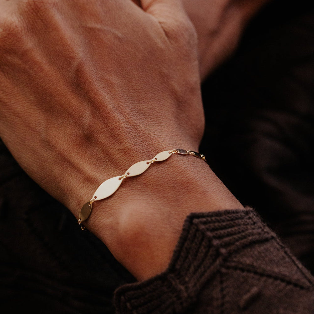 Close-up of a hand wearing a gold bracelet on a dark background