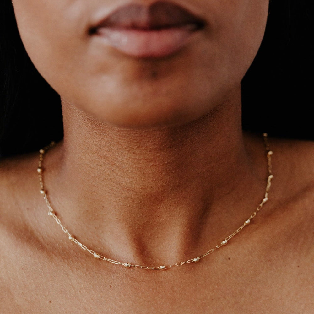 Close-up of a person wearing a gold necklace with a blurred background