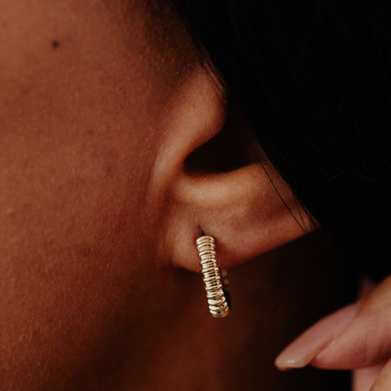 Close-up of an ear wearing a gold hoop earring with a blurred background