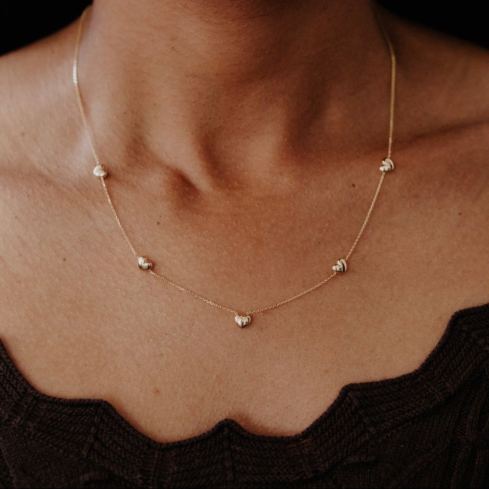 Gold necklace with small heart-shaped pendants on a person wearing a black top.