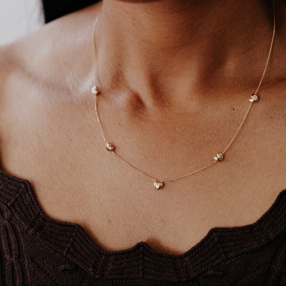 Gold necklace with heart pendants on a person wearing a black top.