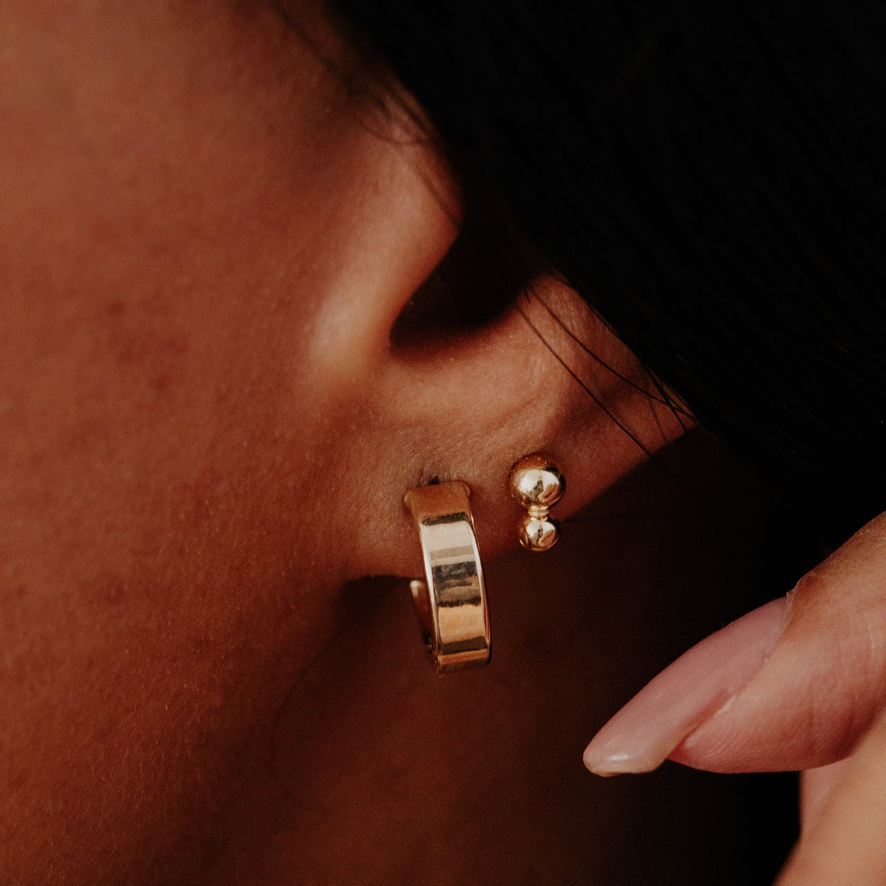 Close-up of a person wearing gold hoop earrings with a blurred background